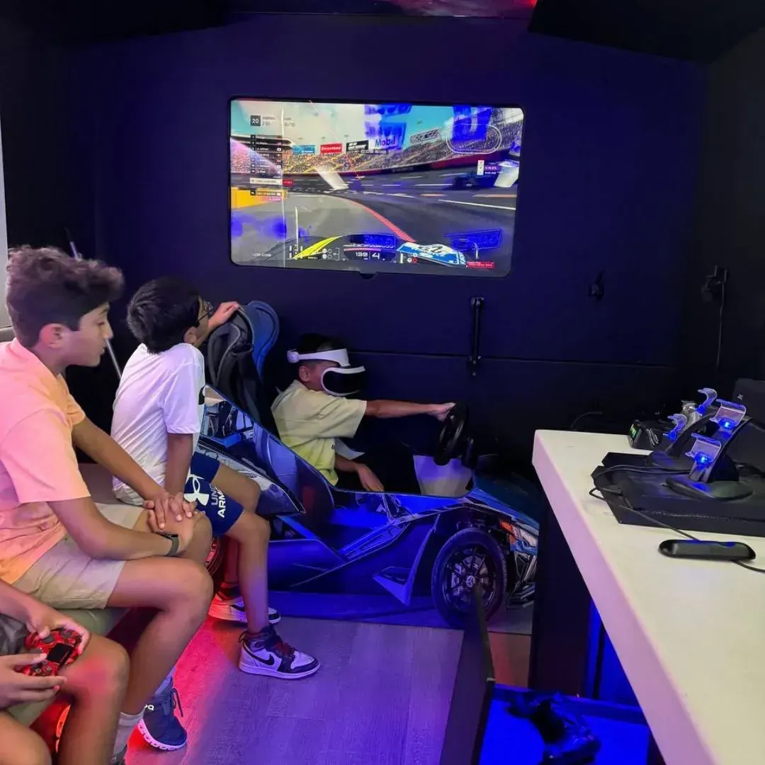 Kid wearing a VR headset driving the racing simulator with friends watching inside the gaming truck
