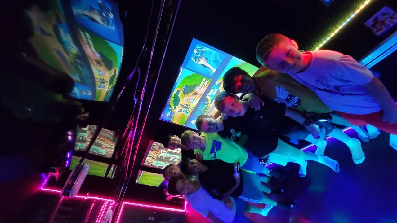 Squad of kids posing for a group photo with PS5 controllers between rounds of Fortnite inside the neon-lit gaming truck