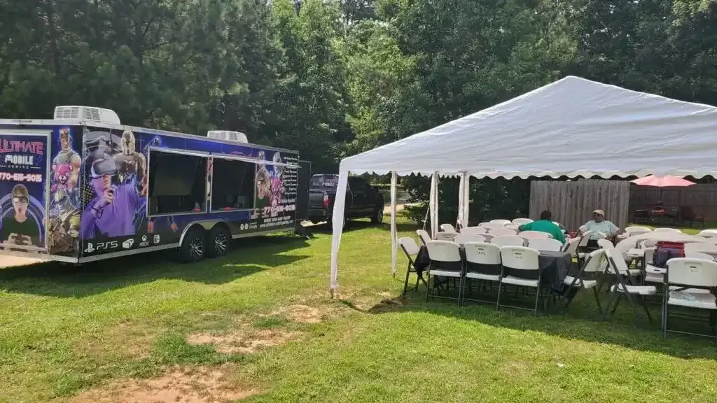 Ultimate Mobile Gaming trailer parked beside a large white event tent with chairs at an outdoor backyard birthday party in Georgia