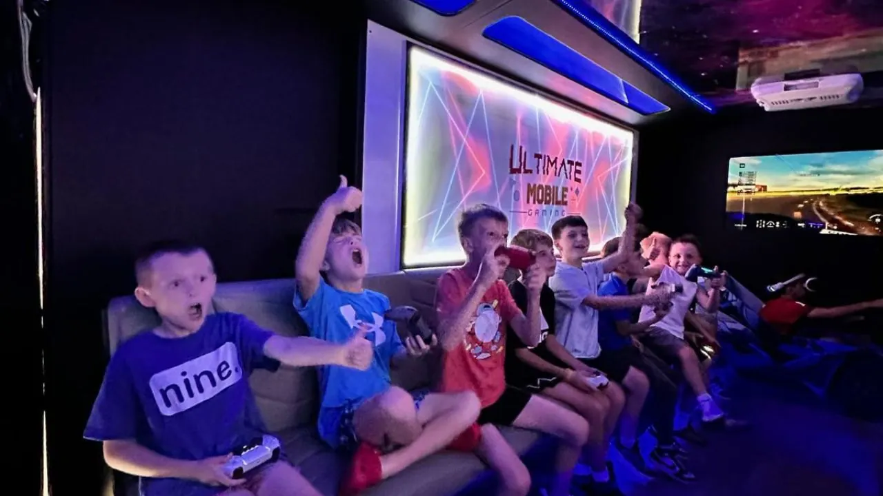 Kids cheering and giving thumbs up while playing video games inside the Ultimate Mobile Gaming truck at an Atlanta birthday party